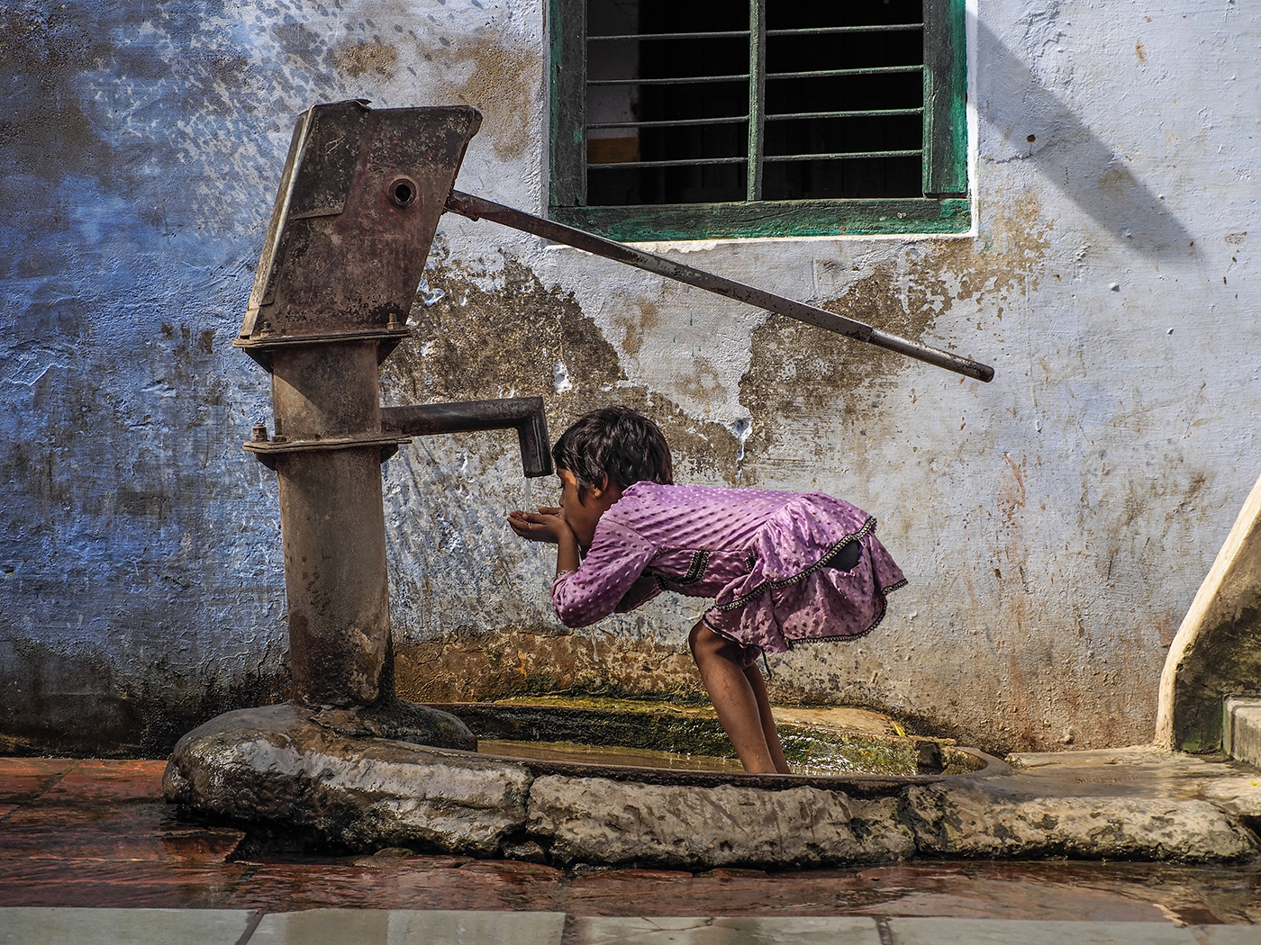 A young girl drinks from village water pump in Kachhpura, India